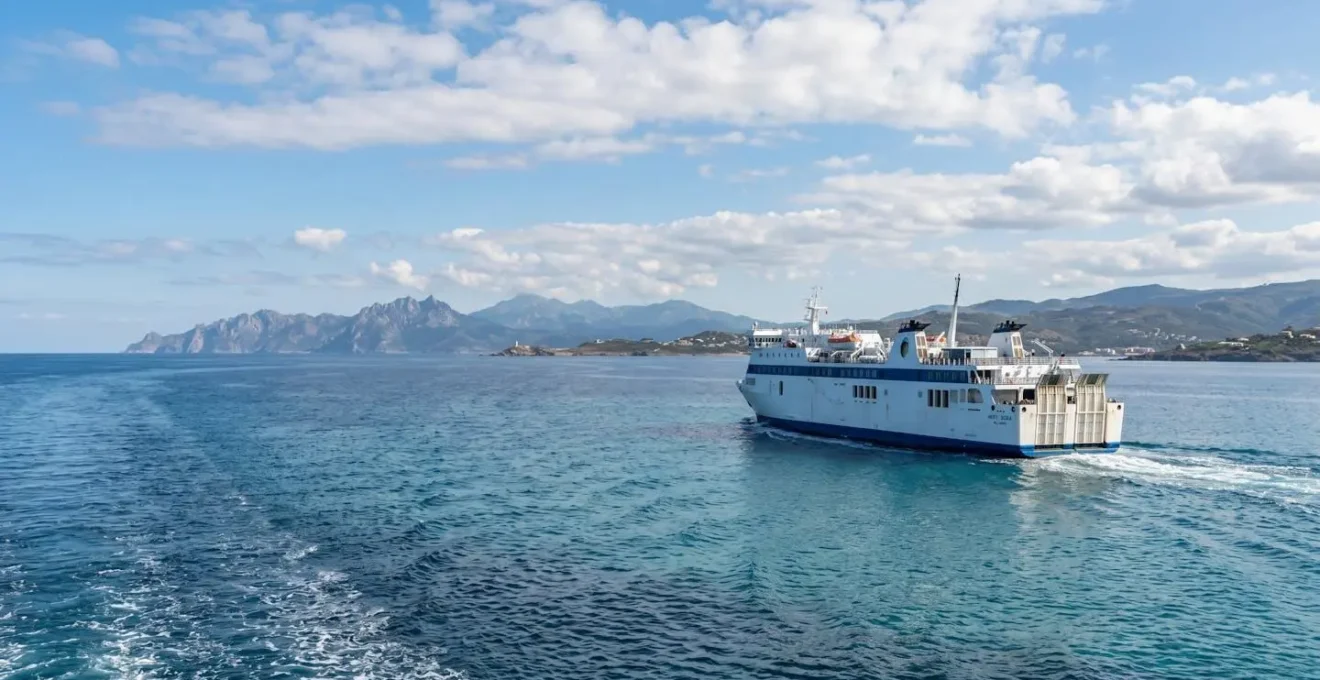 Modernes Fährschiff fährt auf ruhiger See bei hellem Tageslicht, im Hintergrund ist die Küstenlinie Korsikas zu erkennen