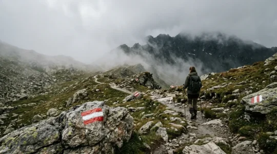 Wanderer folgt rot-weißen Wegmarkierungen auf einem Bergpfad in nebligem alpinem Gelände